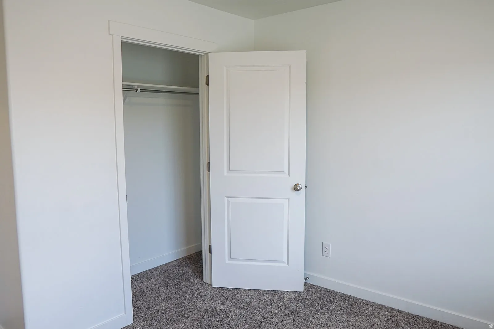 White interior door with brushed nickel hardware, opening to a closet featuring a single hanging rod