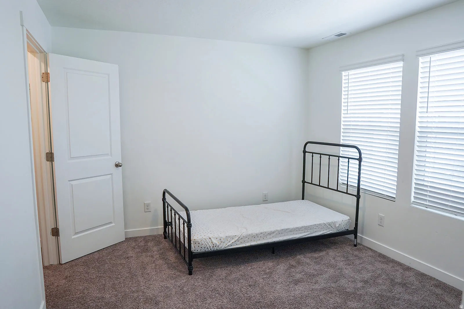 Room featuring neutral wall paint, brown carpet flooring, and two windows with blinds
