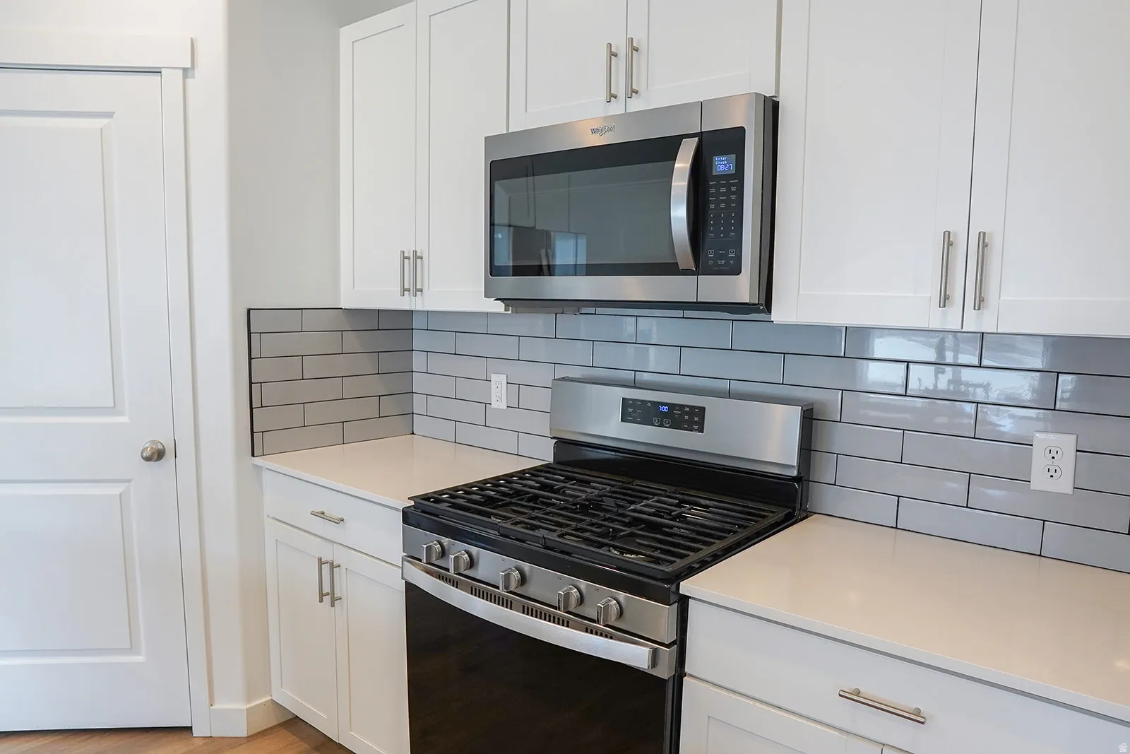 Kitchen featuring a stainless steel gas range, microwave, light gray subway tile backsplash, white shaker-style cabinetry, and light-toned countertops