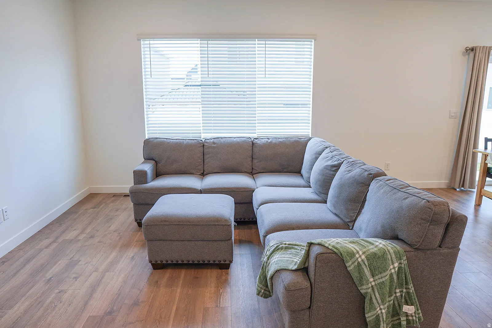 Bright living area featuring wood-finish flooring, white baseboards, and a large window with horizontal blinds