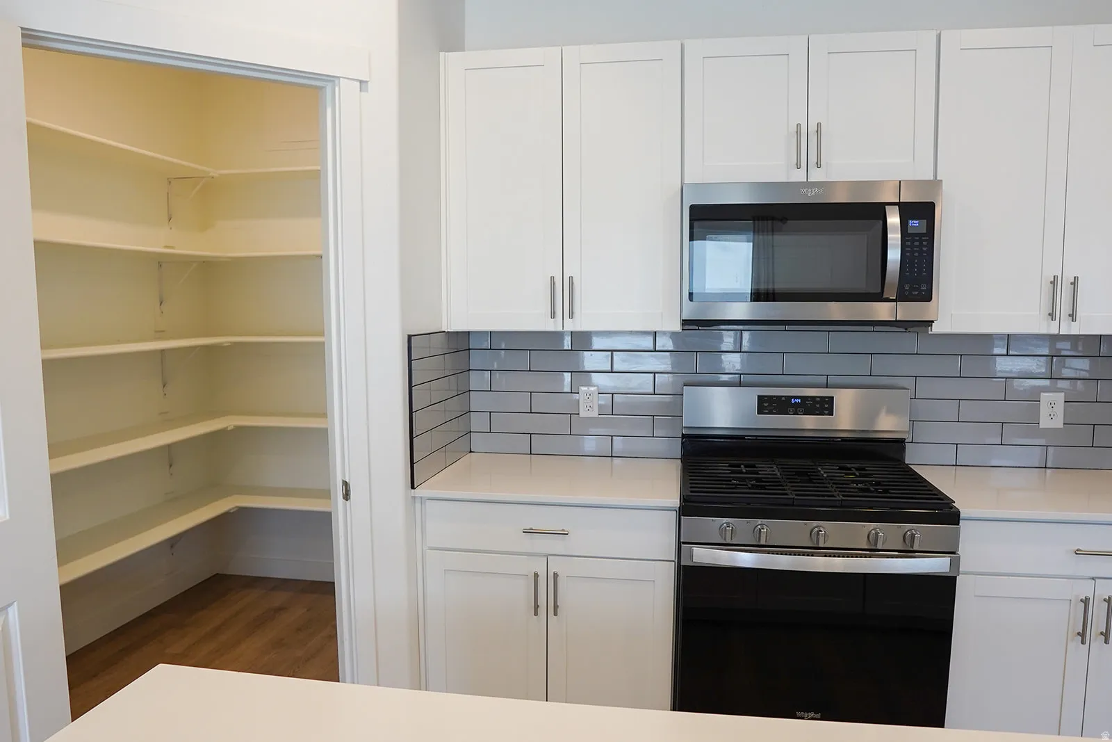 Kitchen featuring white cabinetry, stainless steel appliances, grey subway tile backsplash, and light-toned countertops