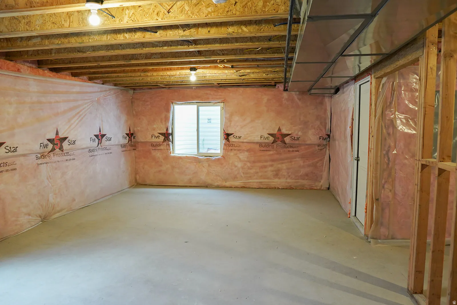 Unfinished basement space featuring exposed wood joists, concrete flooring, perimeter insulation, a single window, and a white interior door