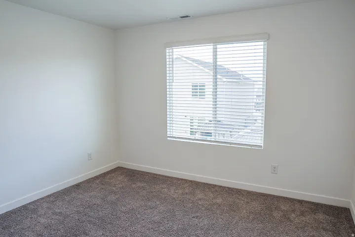 Neutral-toned room featuring a single window with blinds, light-colored walls, and dark-toned carpet