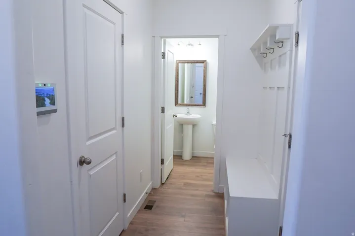 Hallway featuring wood-finish flooring, a built-in hall tree with bench, and access to a bathroom with a pedestal sink and framed mirror