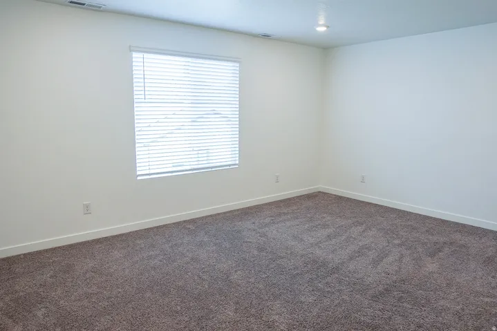 Spacious room featuring neutral carpeting, white walls, and a large window with horizontal blinds