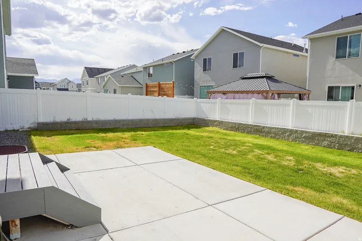 Expansive backyard featuring a concrete patio, composite deck steps, and a white vinyl privacy fence atop a stone retaining wall