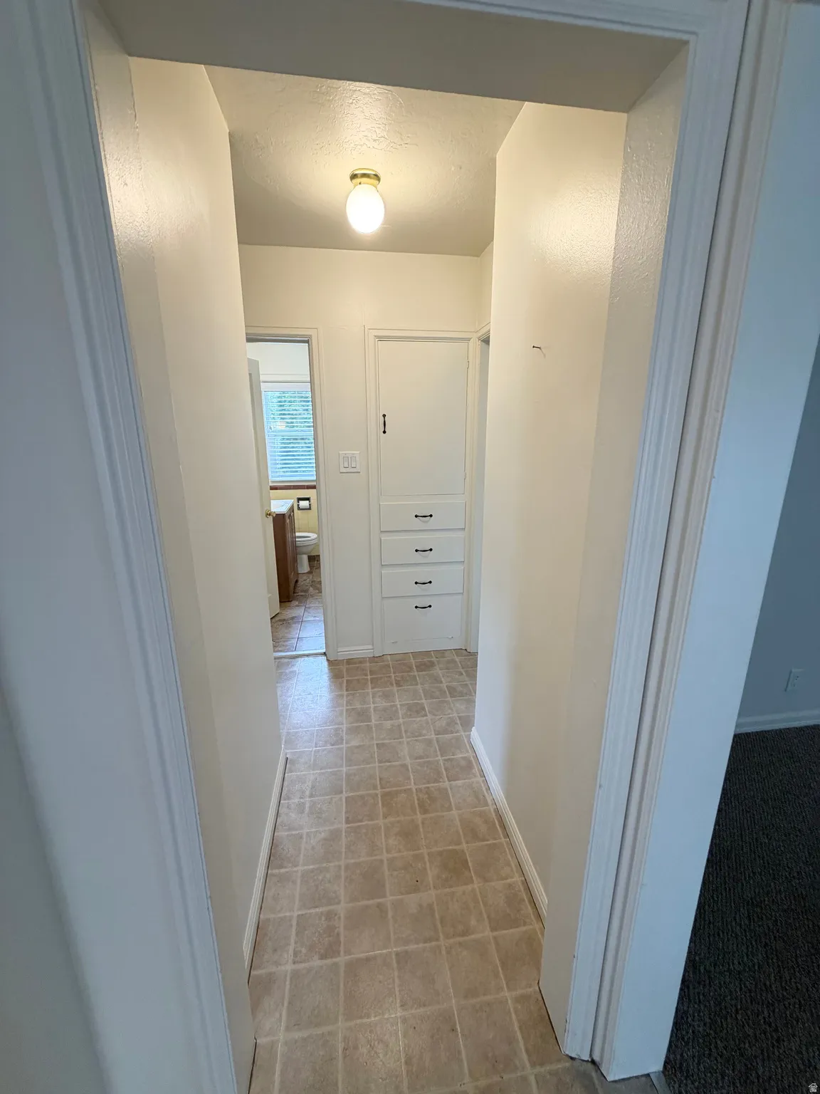 Hallway featuring square tile flooring, built-in storage cabinetry with four drawers, a ceiling-mounted light fixture, and neutral painted walls