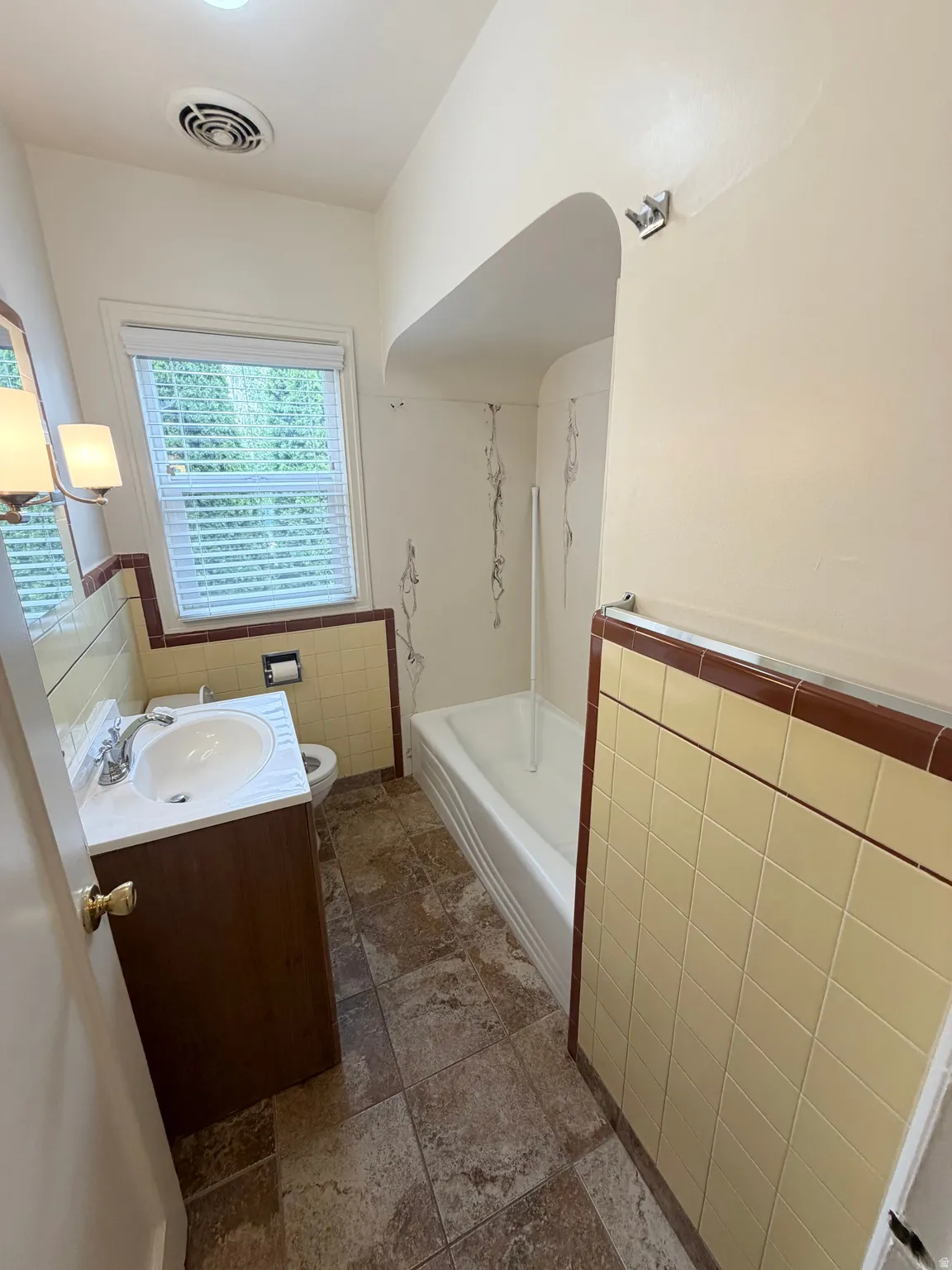 Bathroom featuring a white bathtub, ceramic wall tiling, a vanity with an integrated sink, and a window with blinds