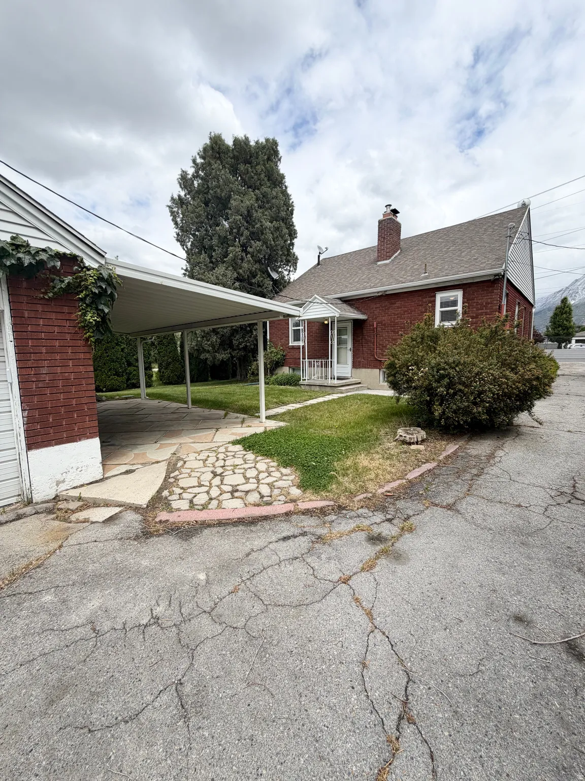 Brick exterior property featuring a carport, a paved driveway, and a front entrance with a small porch