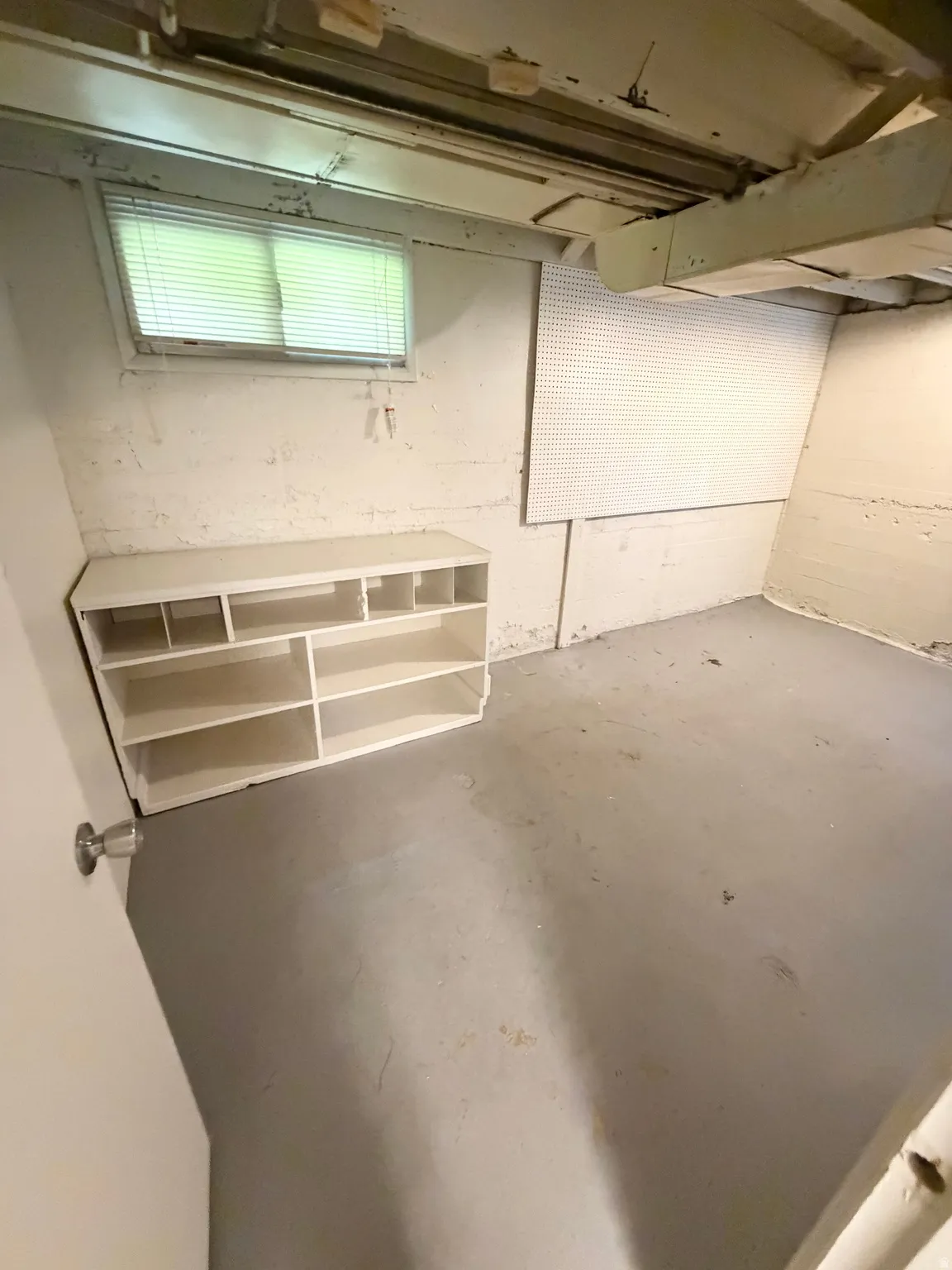 Basement area featuring a painted concrete floor, exposed ceiling joists, and a built-in shelving unit