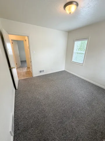 Carpeted interior room featuring a window with blinds, white walls, and a ceiling-mounted light fixture