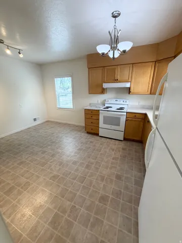 Kitchen featuring natural wood-finish cabinetry, white appliances, and a tiled floor