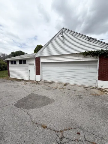 Detached garage featuring white horizontal siding, a red brick facade, a white paneled garage door, and a dedicated side entrance