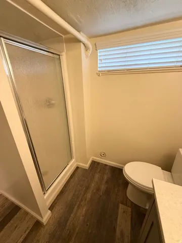 Three-quarter bath featuring a glass-enclosed shower, wood-finish flooring, and a window with blinds