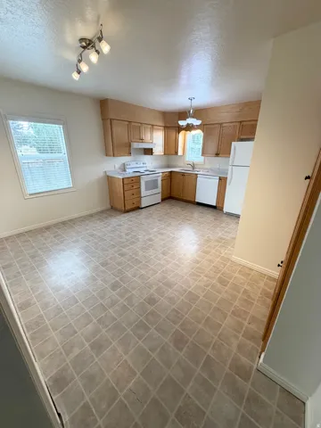 Open-concept kitchen and dining area featuring light wood cabinetry, white appliances, and a durable tile-patterned floor