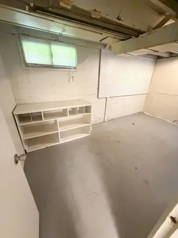 Basement area featuring a painted concrete floor, exposed ceiling joists, and a built-in shelving unit