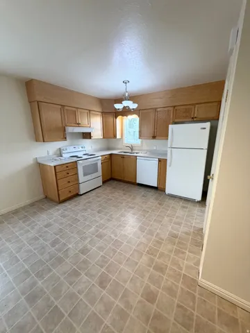Kitchen featuring wood-finish cabinetry, white appliances, and a corner sink