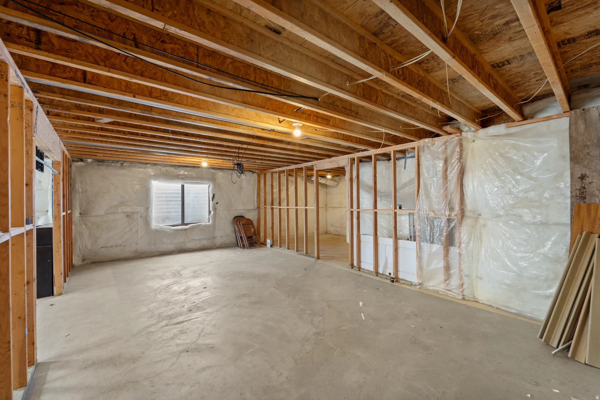 Unfinished basement featuring exposed wood joists, concrete flooring, framed wall sections, and a window opening with a security grate