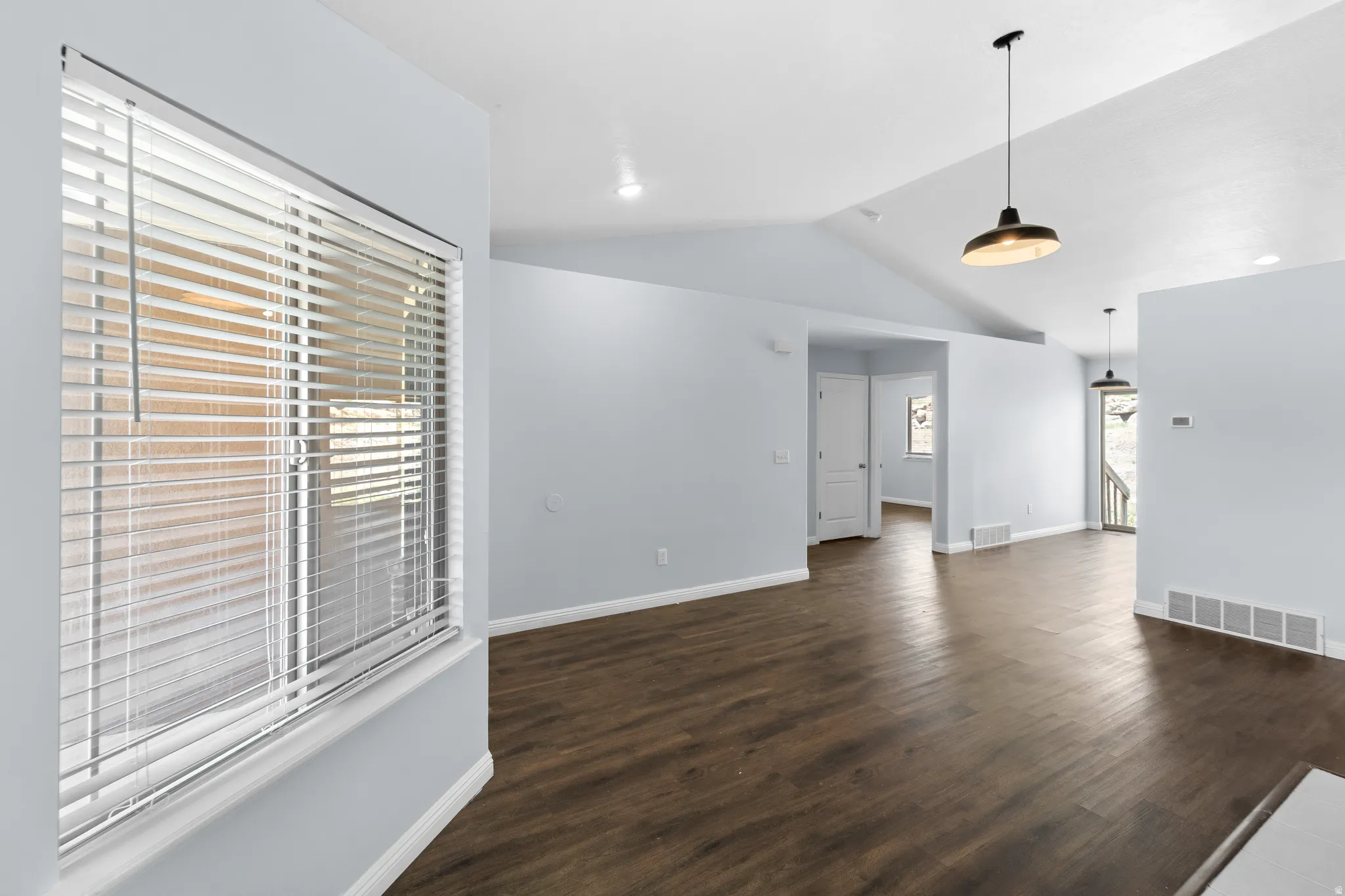 Spacious room featuring vaulted ceilings, wood-finish flooring, and light gray walls