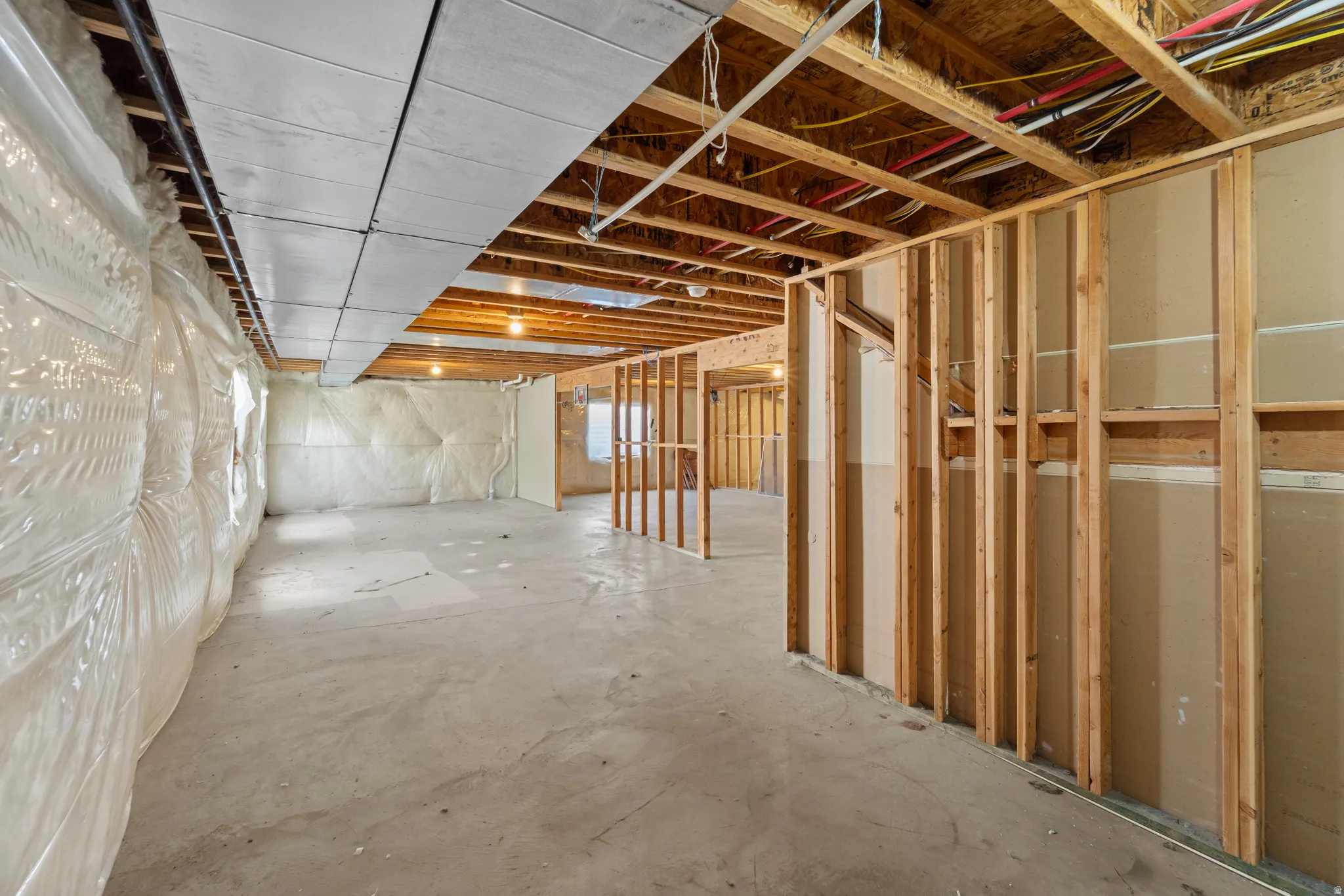 Unfinished basement with concrete flooring, exposed wood ceiling joists, and framed partition walls