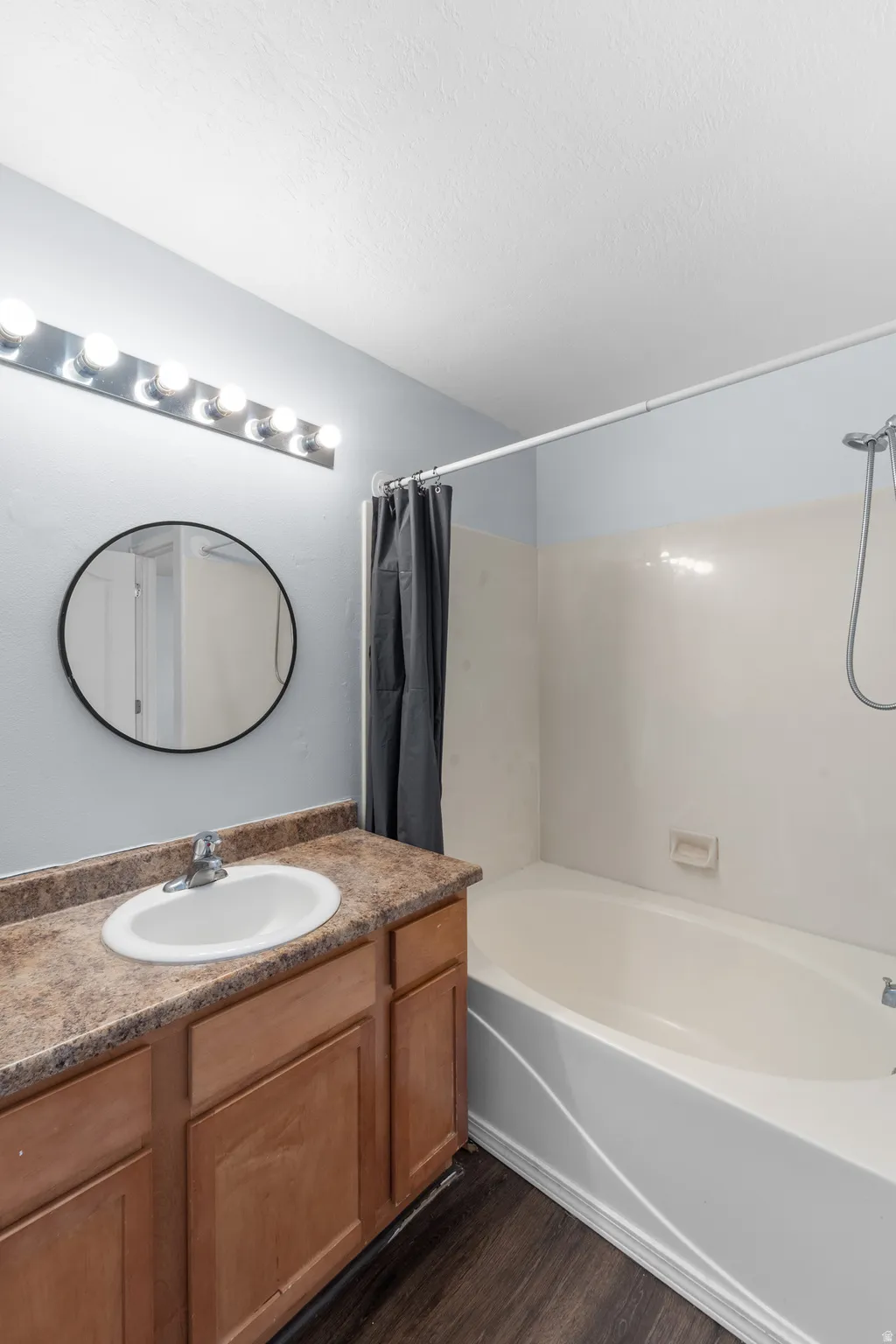 Bathroom with wood-finish flooring, a white bathtub, and a wood vanity with a single basin sink