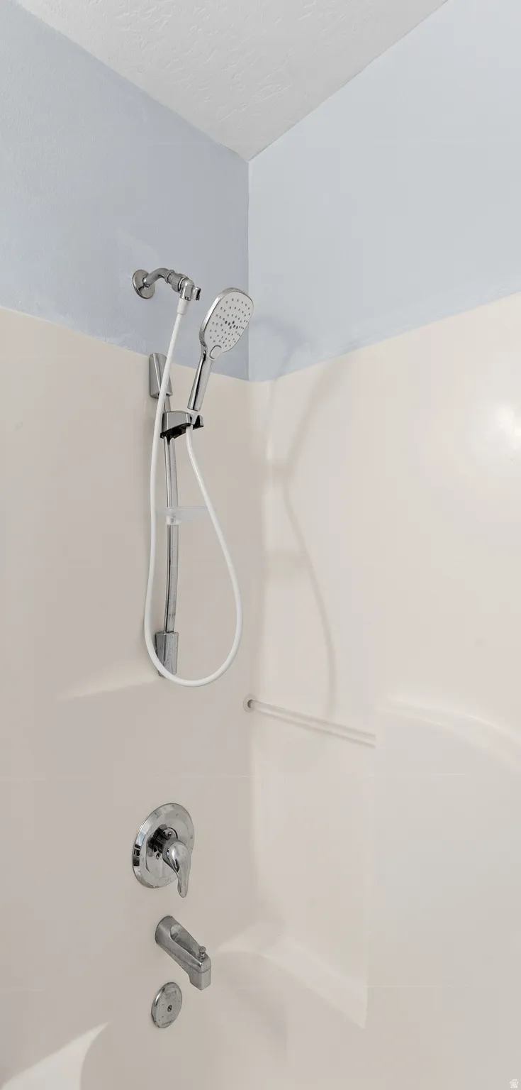 Bathtub with integrated shower surround, featuring a handheld shower head, chrome fixtures, and a textured white ceiling