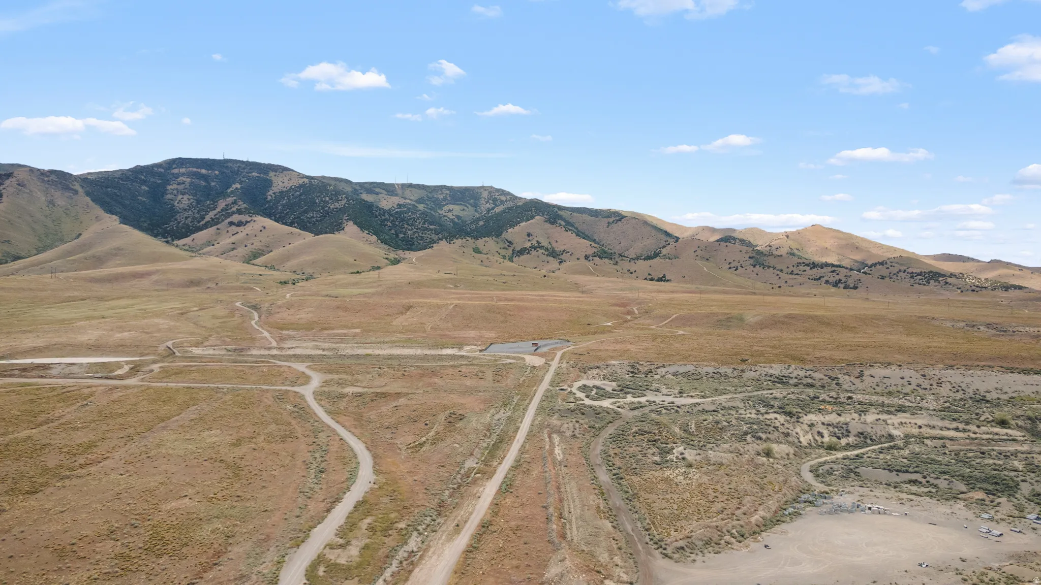 Expansive undeveloped land with a mountainous backdrop, featuring natural terrain and visible dirt roads