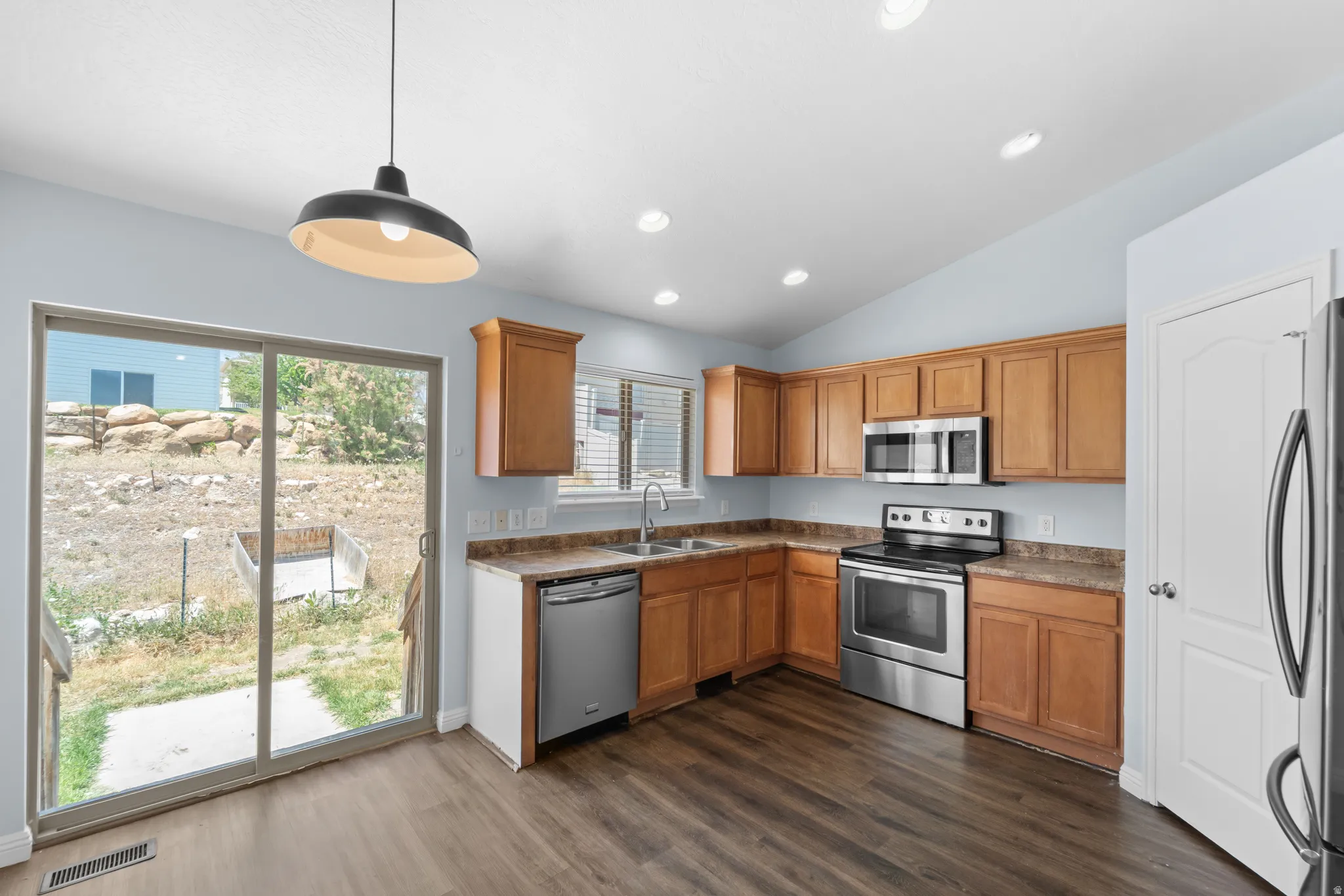 Kitchen featuring wood-finish flooring, oak cabinetry, stainless steel appliances, and a sliding glass door