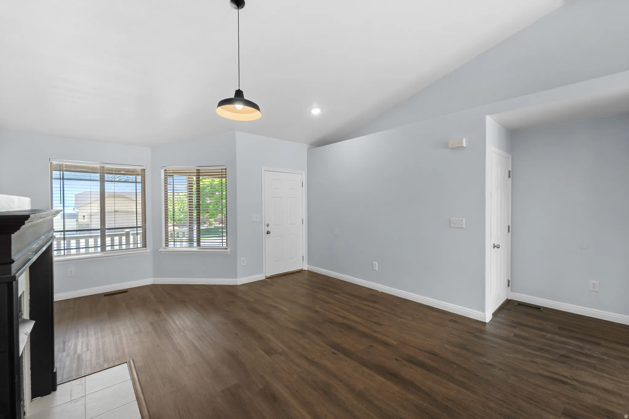 Spacious room featuring vaulted ceilings, wood-finish flooring, a contemporary pendant light fixture, and multiple windows with blinds