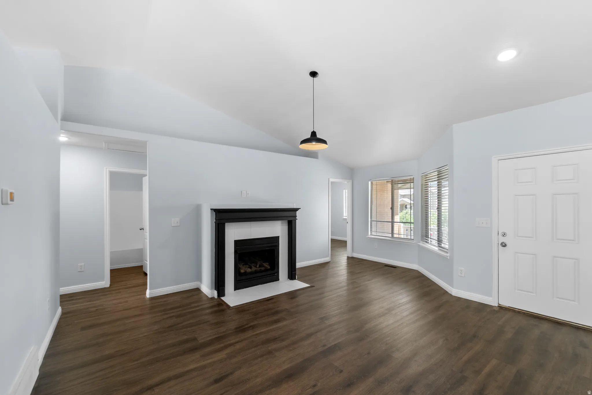 Spacious living area featuring vaulted ceilings, wood-finish flooring, a fireplace with a black wood mantel and white tile surround, and large bay windows