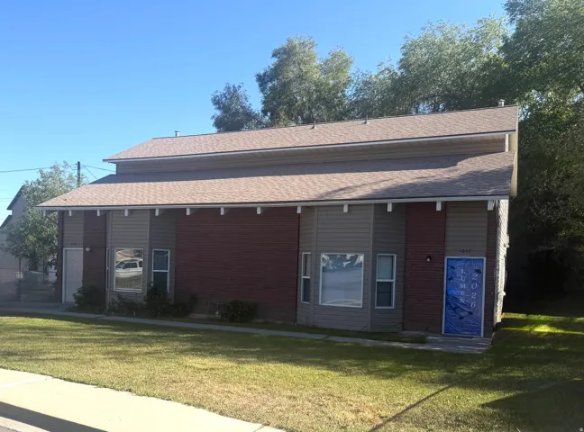 Multi-unit building featuring a gabled roof with brown shingles, a combination of red brick siding and gray horizontal siding, and multiple windows
