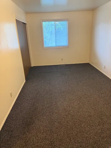 Bright room featuring neutral-toned walls, a window with horizontal blinds, and dark speckled carpeting