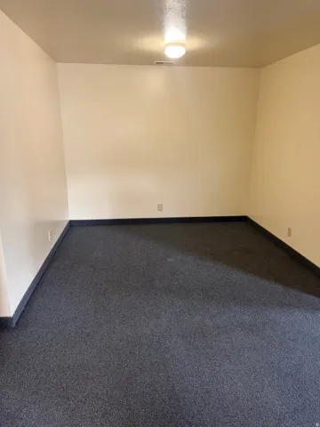 Spacious room featuring neutral painted walls and dark carpet flooring