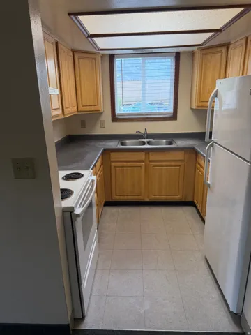 U-shaped kitchen featuring light wood cabinetry, dark countertops, a double basin sink, and a white electric range
