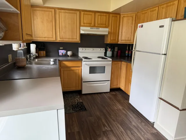 Well-appointed kitchen featuring wood cabinetry, dark countertops, white appliances, and wood-finish flooring