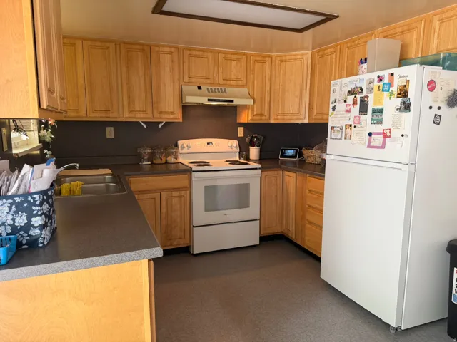 Kitchen featuring light wood cabinetry, dark countertops, white electric range, and a double basin stainless steel sink