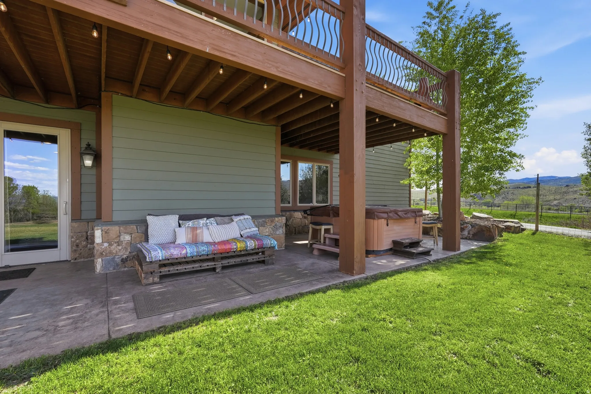 Expansive concrete patio featuring a hot tub, a full-light exterior door, and string lighting