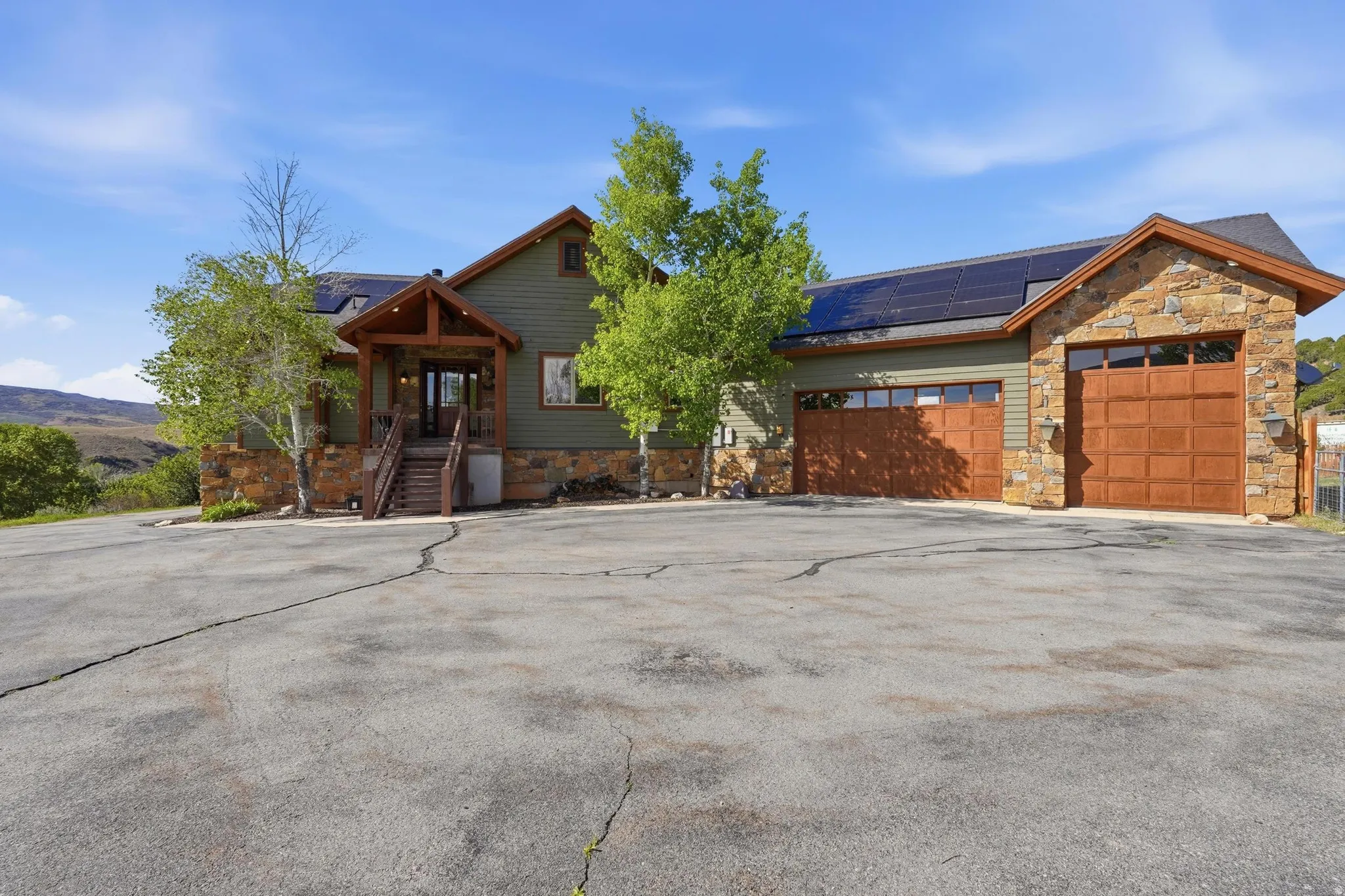 Craftsman-style home featuring a stone and siding exterior, integrated solar panels, a covered entry porch with wood columns, and a multi-car garage with wood-finish doors
