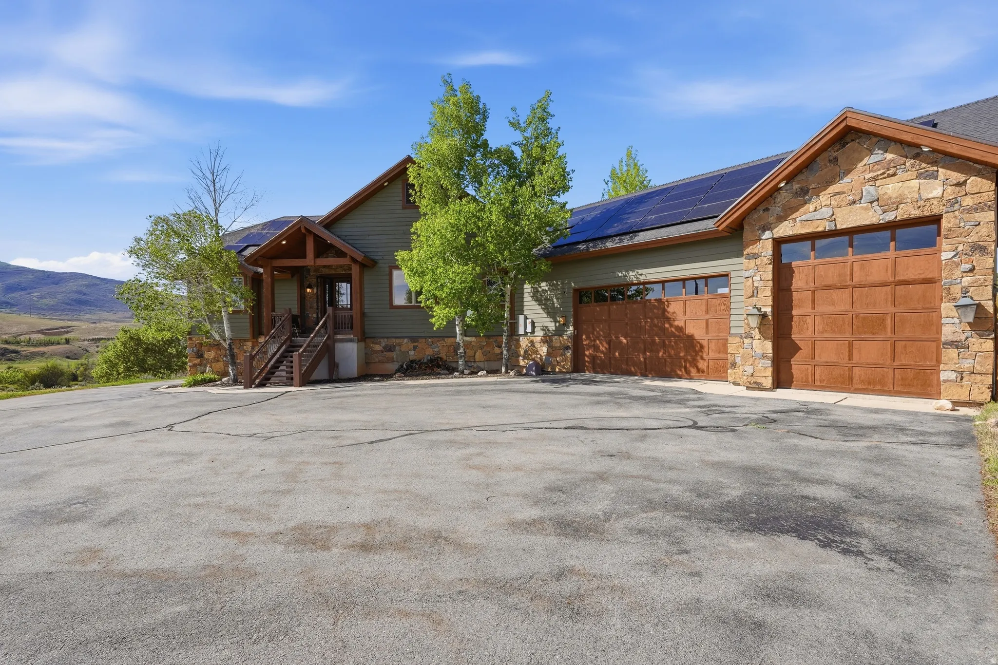 Craftsman-style home featuring a stone and siding exterior, integrated solar panels, a covered entry porch with wood railings, and two attached garage bays with wood-finish doors
