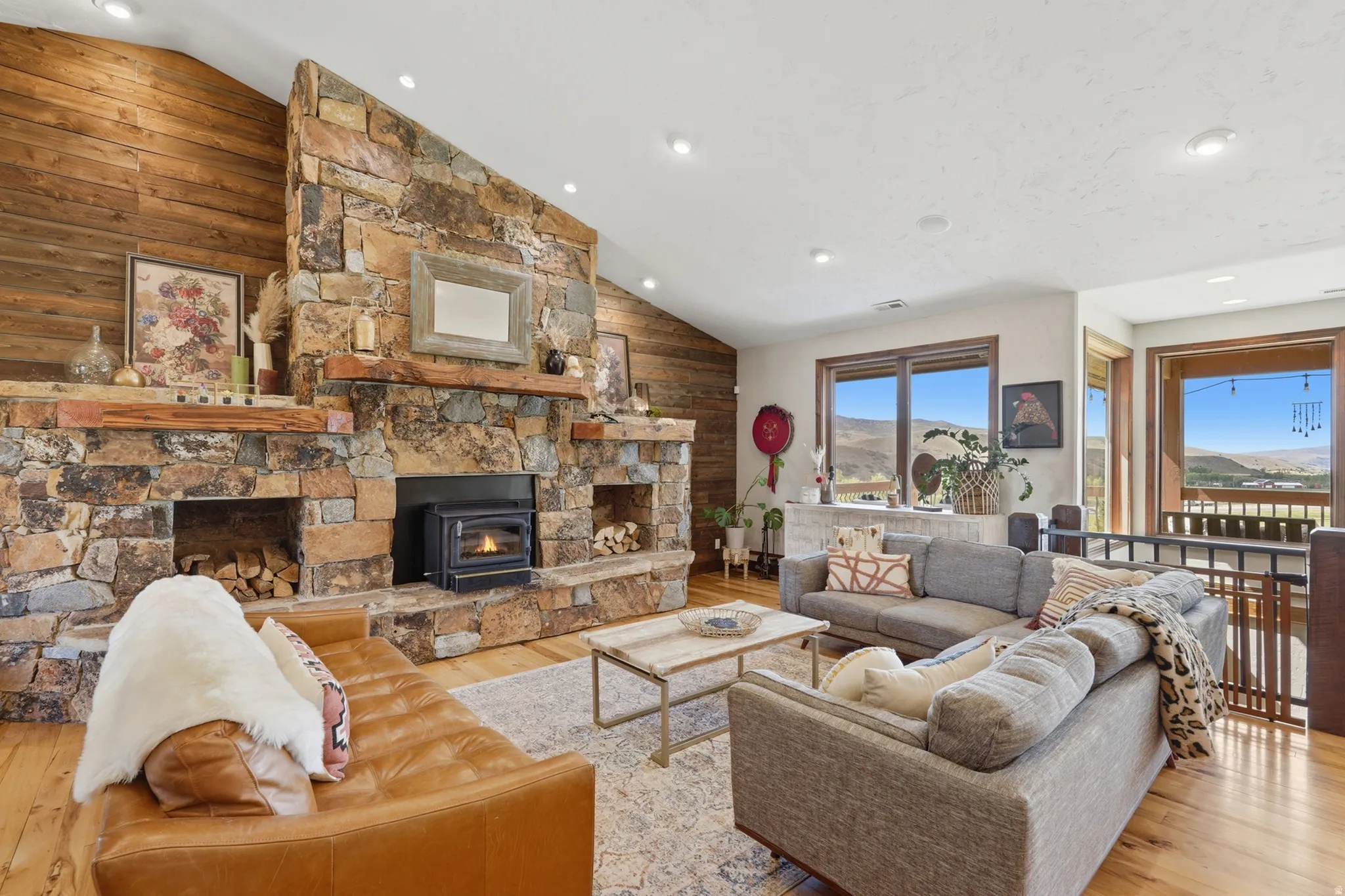 Vaulted ceilings with recessed lighting complement a floor-to-ceiling stone fireplace featuring a wood-burning insert and integrated wood storage
