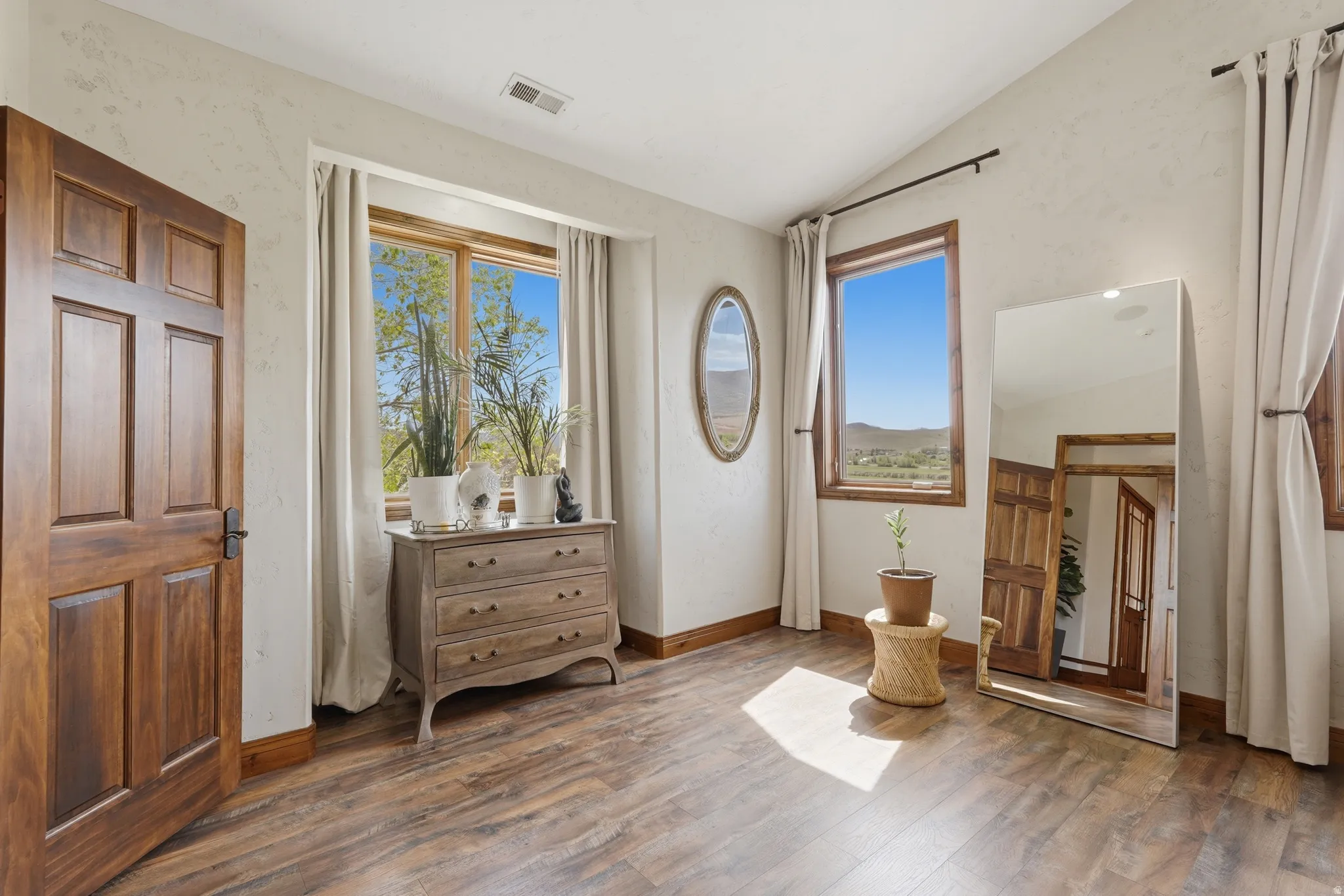 Spacious room featuring wood-finish flooring, multiple windows with wood trim, and a vaulted ceiling