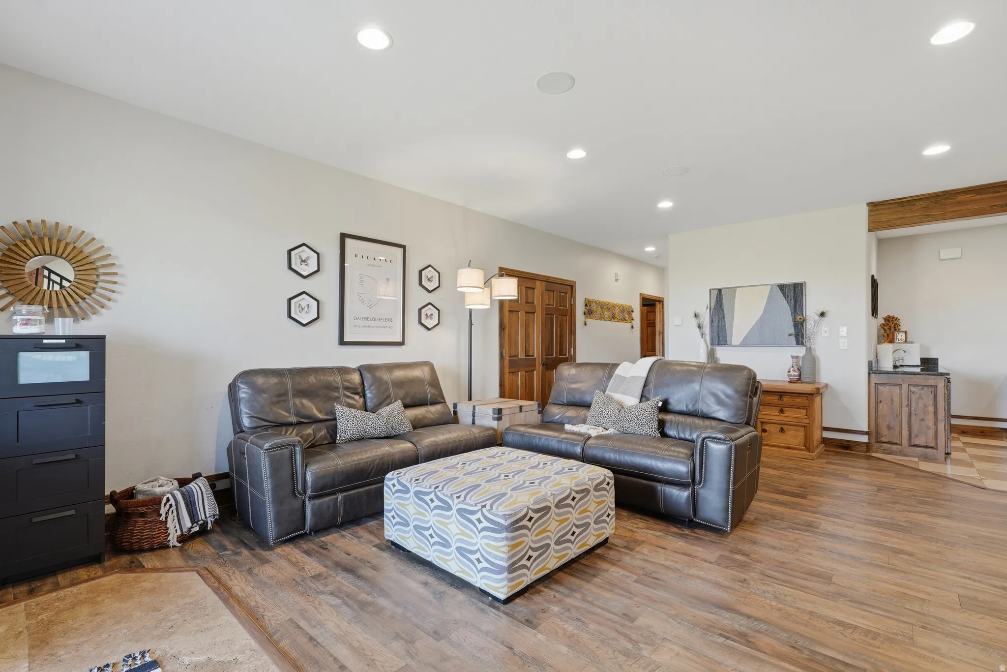 Spacious living area featuring wood-finish flooring, recessed ceiling lighting, light neutral wall tones, and rich wood doors