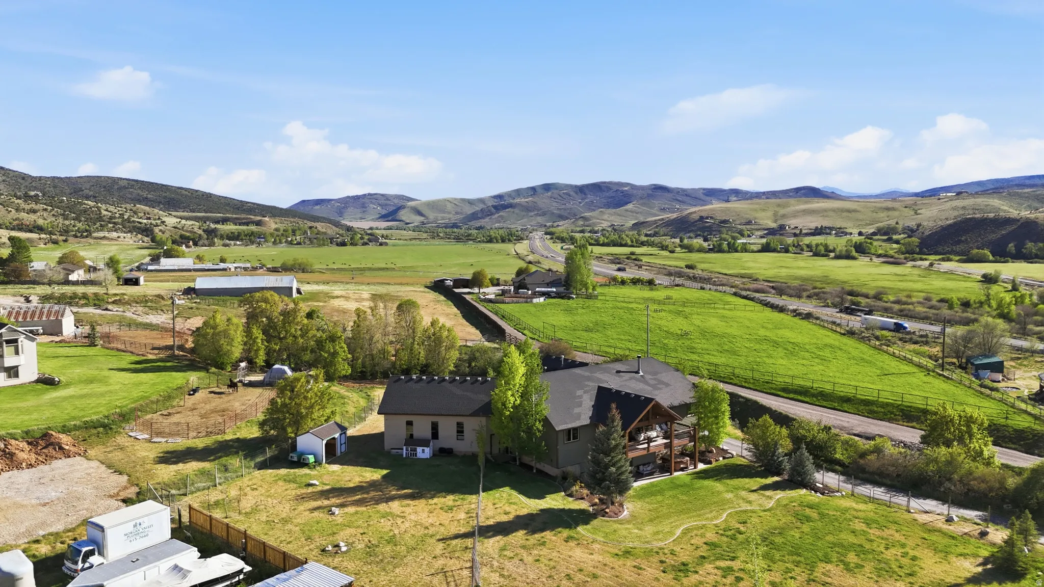 Expansive rural property featuring multiple structures, verdant fields, mature trees, and mountainous topography
