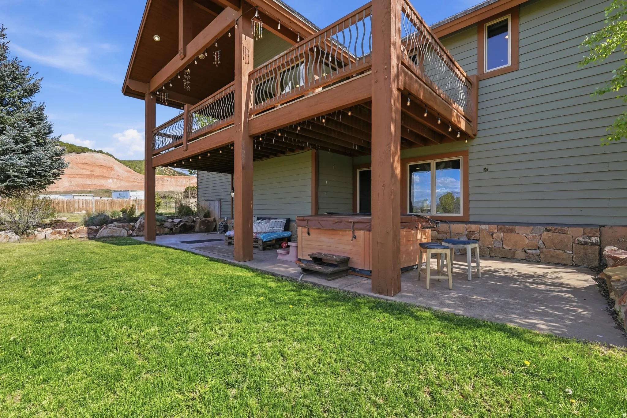 Expansive backyard featuring a manicured lawn, a two-story wood deck, a patio with a hot tub, and a stone retaining wall