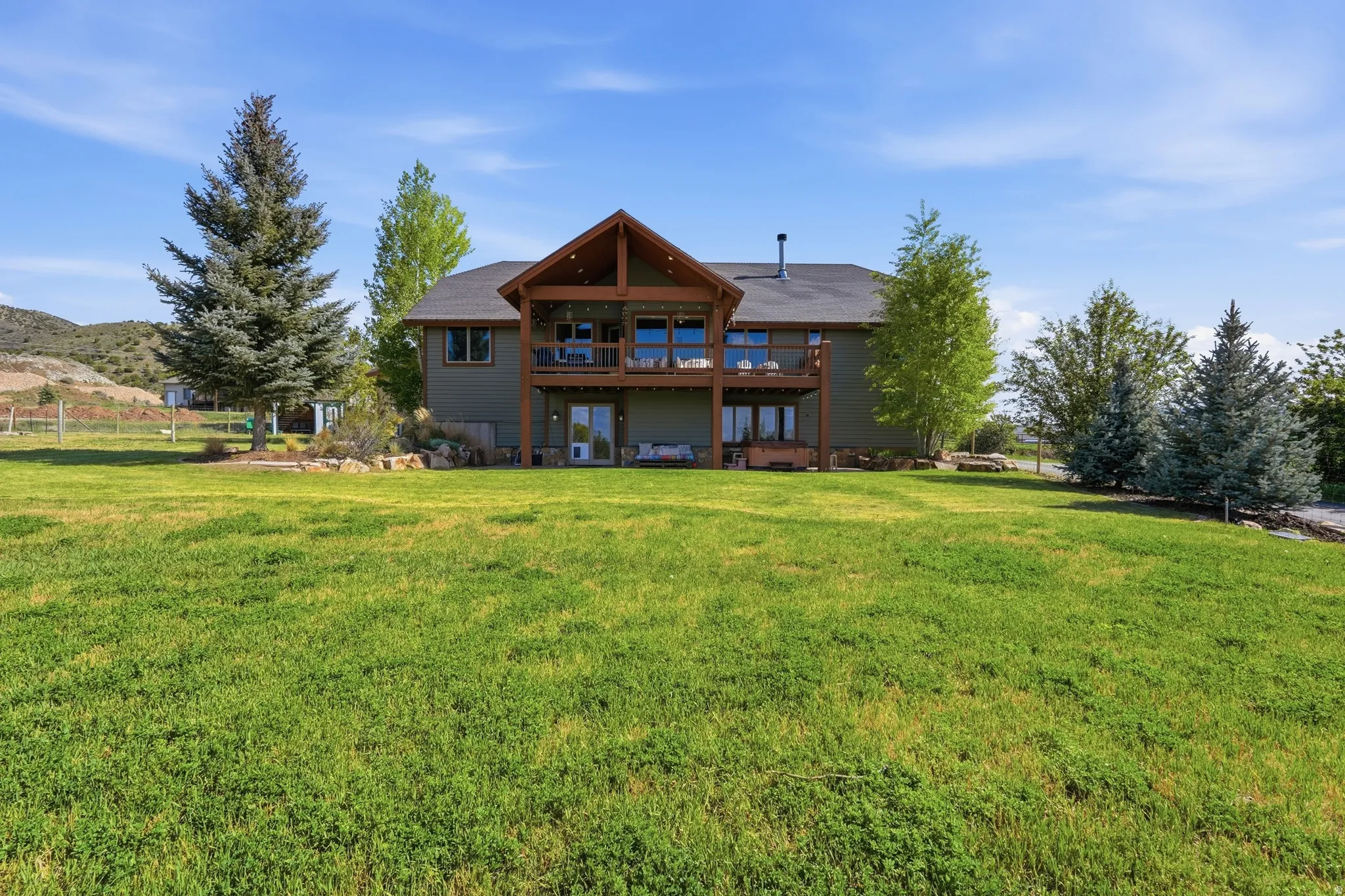 Spacious rear lawn with mature trees bordering a two-story home featuring a full-width upper deck and a lower patio