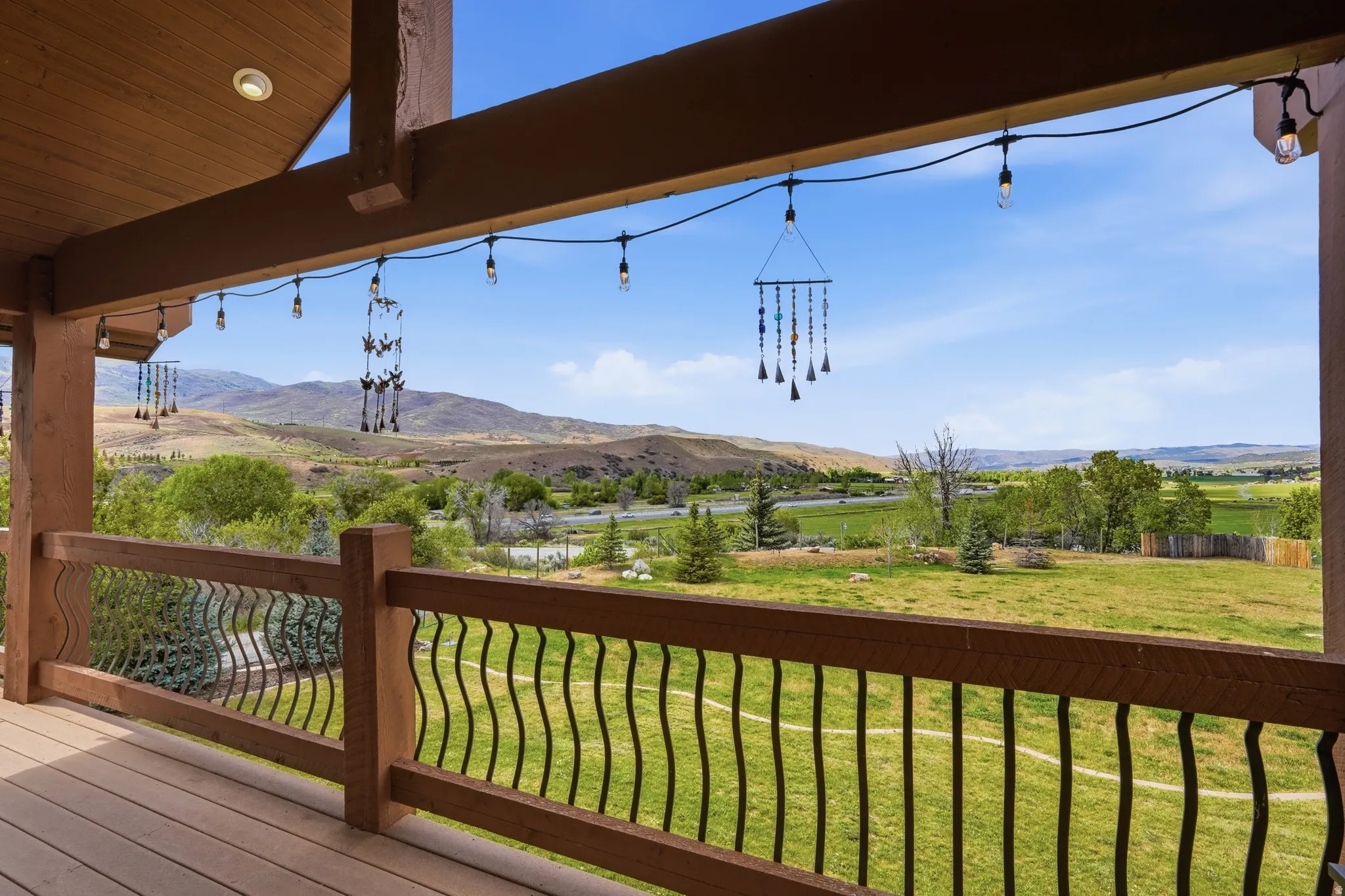 Covered outdoor deck with wood-finish flooring, exposed wood beams, and a black wrought iron railing