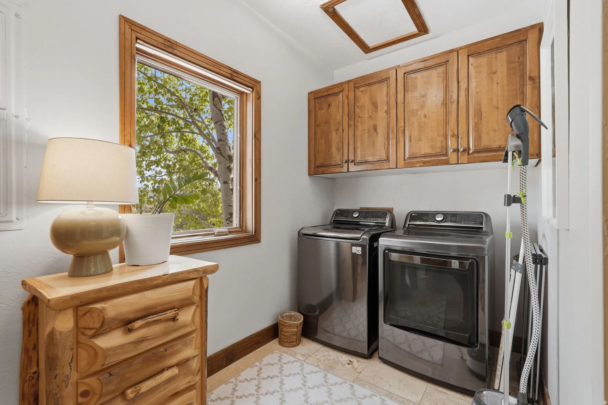 Laundry area featuring wood-finish cabinetry, a large window with natural wood trim, and tile flooring with a patterned rug