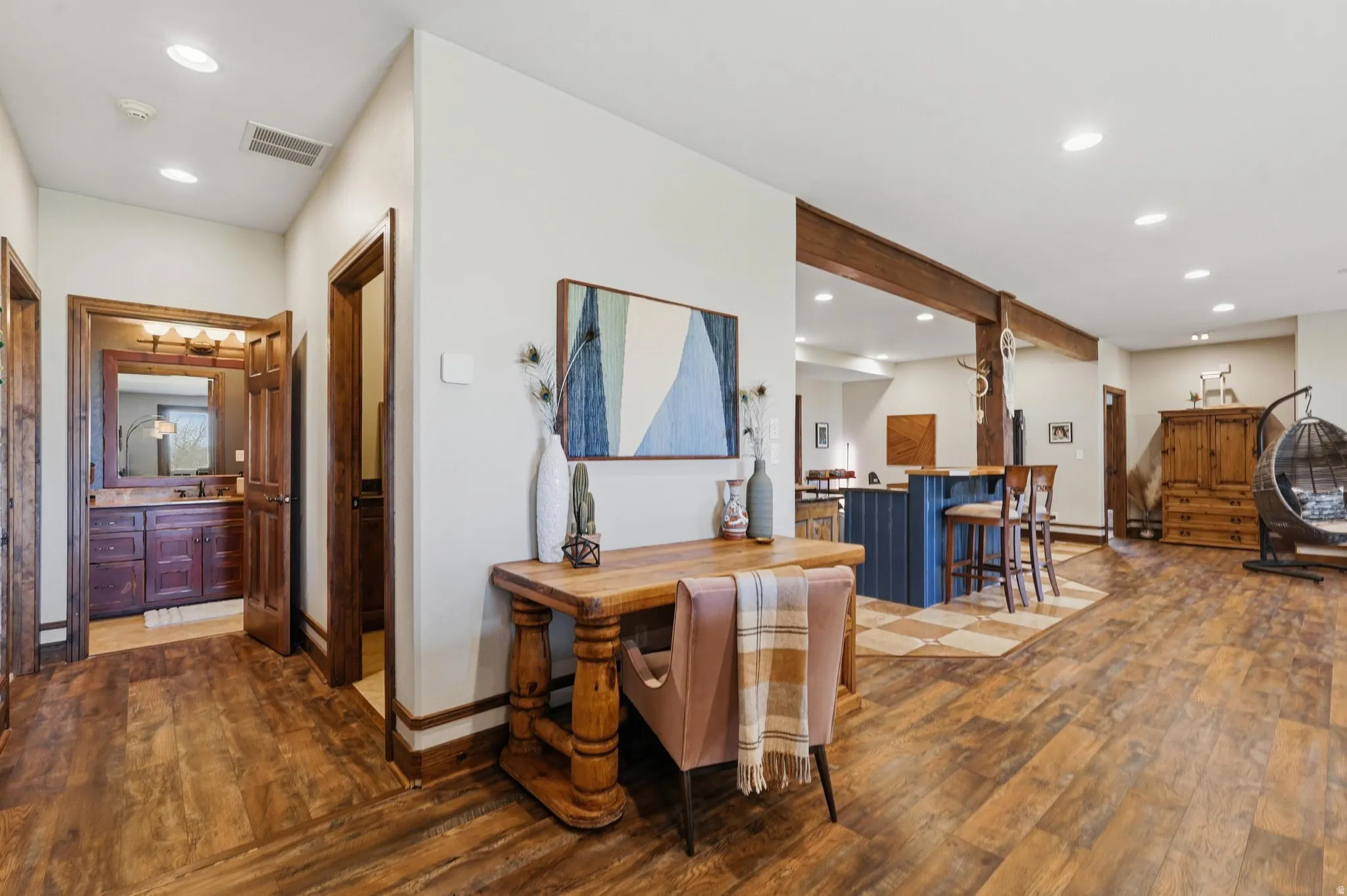 Wood-finish flooring throughout, featuring a hallway with a visible bathroom vanity and a recreation area with a built-in bar