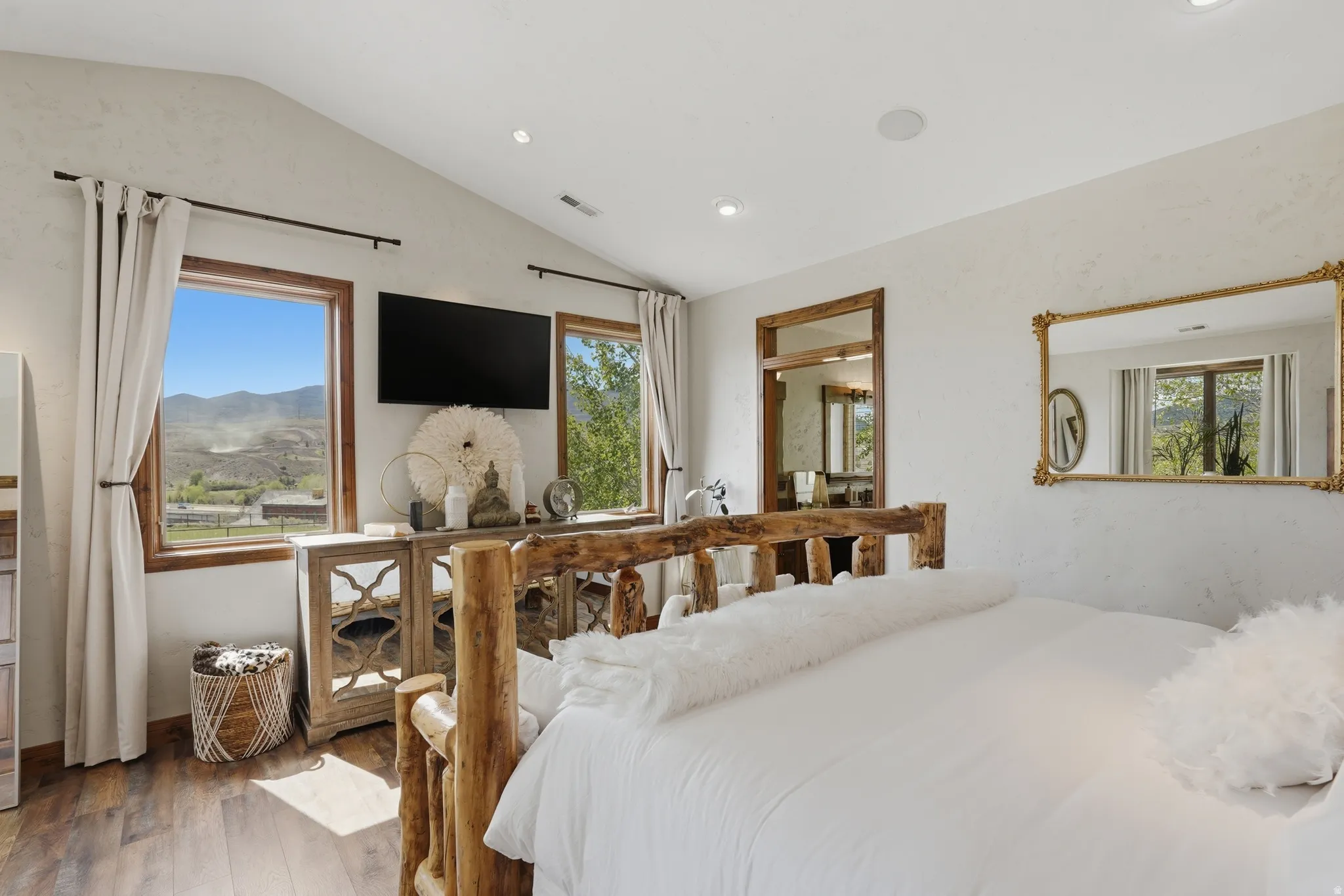 Vaulted ceilings featuring recessed lighting, wood-finish flooring, two large windows with natural wood trim, and an attached wall-mounted television