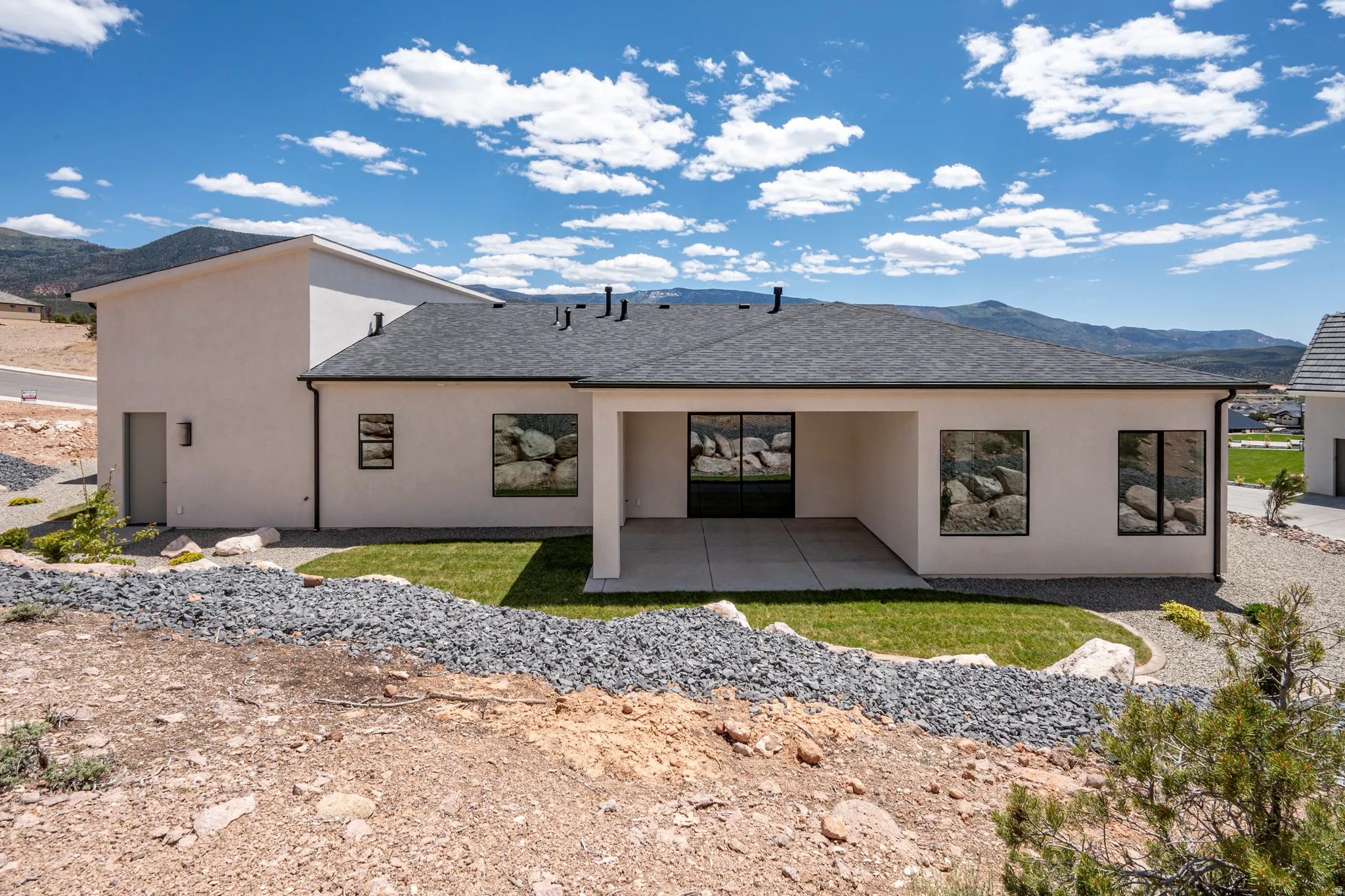 Contemporary rear exterior featuring a covered patio with concrete flooring, stucco siding, and a dark shingle roof